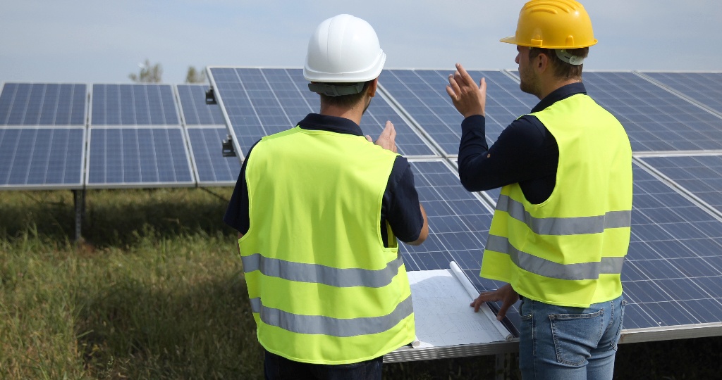 Deux hommes de dos dans une ferme solaire, portant des gilets de sécurité, réunion de chantier